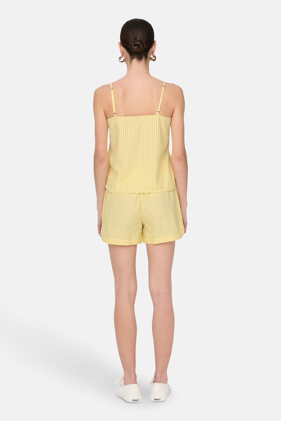 Gele mouwloze blouse van JDY, met verticale strepen, gedragen met een bijpassende korte broek en witte schoenen.