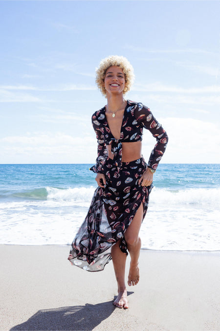 Zwarte blouse met lange mouwen van ONLY, met schelpdessin, gedragen met een bijpassende rok op een strand.