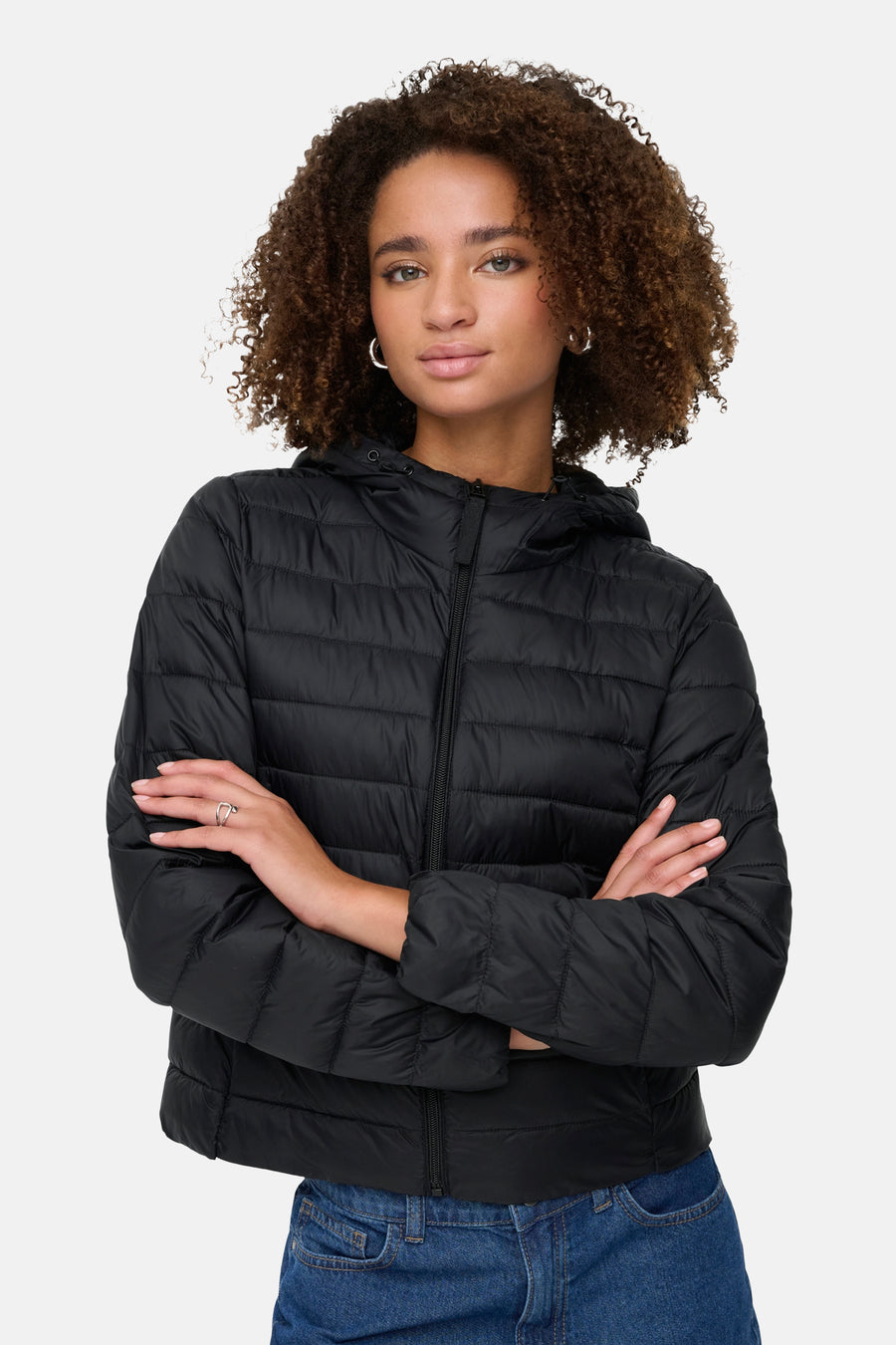 Zwarte regenjas van ONLY®, gedragen door een vrouw met gekruiste armen, met zichtbare jeans.