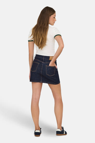 Korte donkerblauwe spijkerrok van ONLY, gedragen met een wit T-shirt met groene randen en sneakers.
