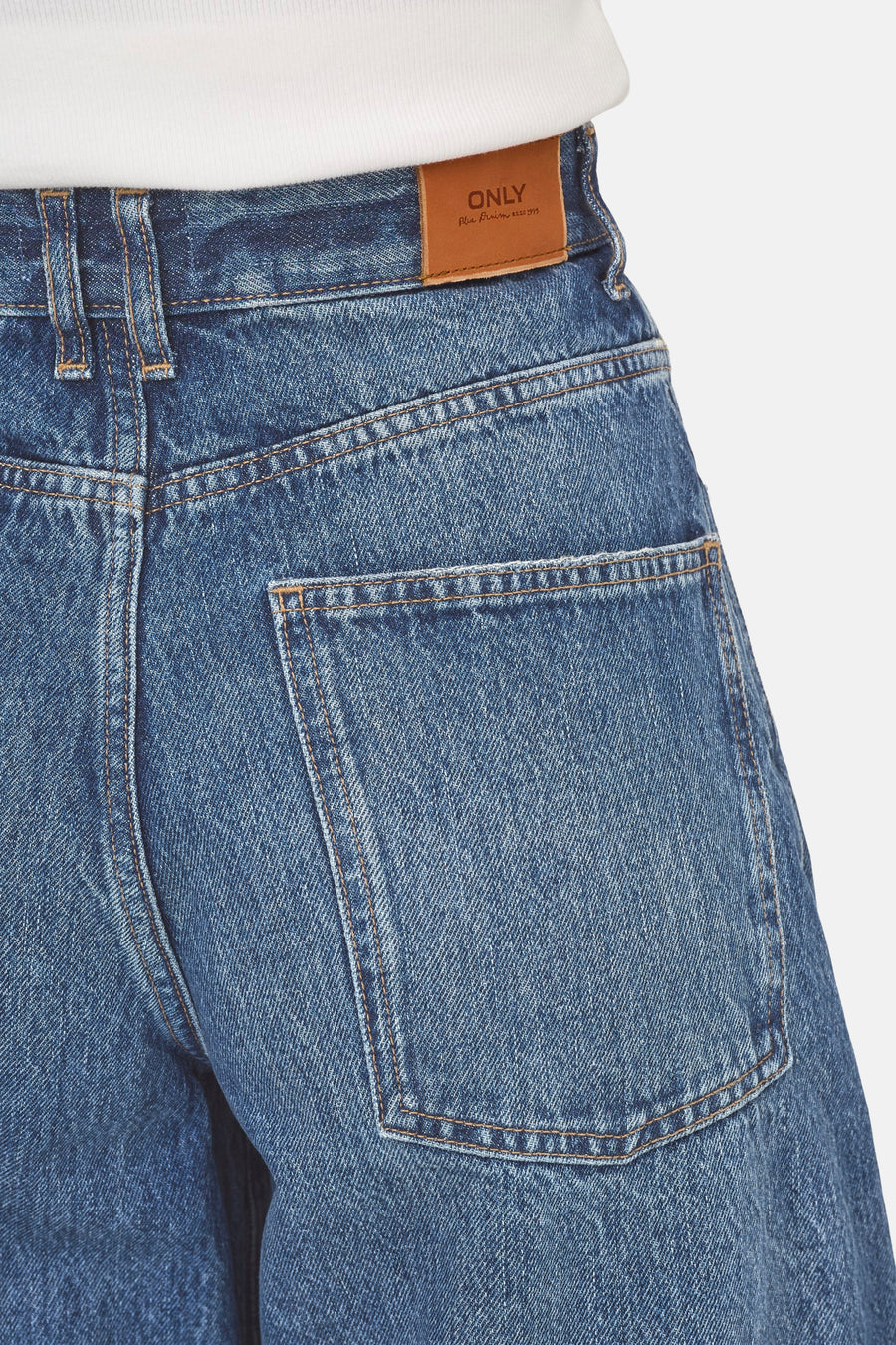 Dark blue denim jeans by ONLY, featuring back pocket with brown stitching and leather brand patch, worn with white ribbed top.