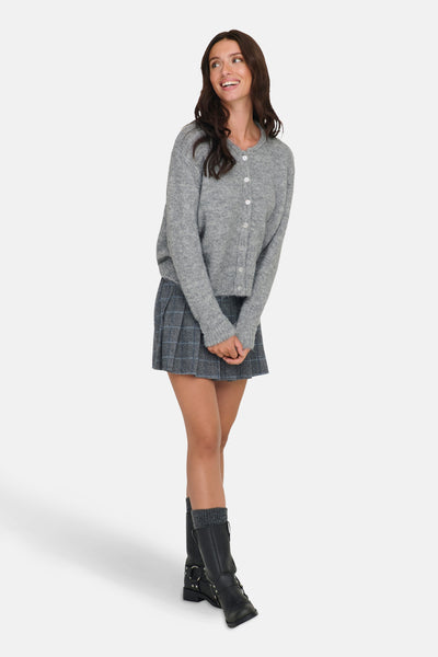 Cardigan gris de ONLY, porté avec une jupe plissée à carreaux et des bottes noires.

