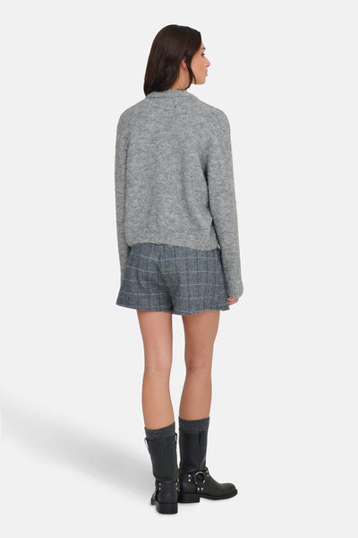 Cardigan gris chiné de ONLY®, porté avec un short à carreaux et des bottes noires.
