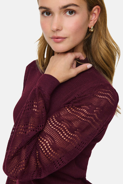 Pull bordeaux à manches ajourées de ONLY, porté avec un bijou d'oreille doré.
