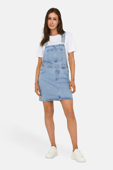 Lichtblauwe spijkerjurk van ONLY, gedragen over een wit T-shirt en witte sneakers.