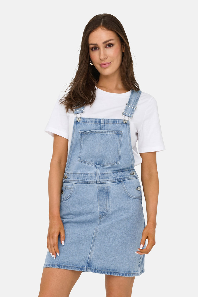Lichtblauwe spijkerjurk van ONLY, gedragen over een effen wit T-shirt, met zilverkleurige bandjes en knoopdetails.
