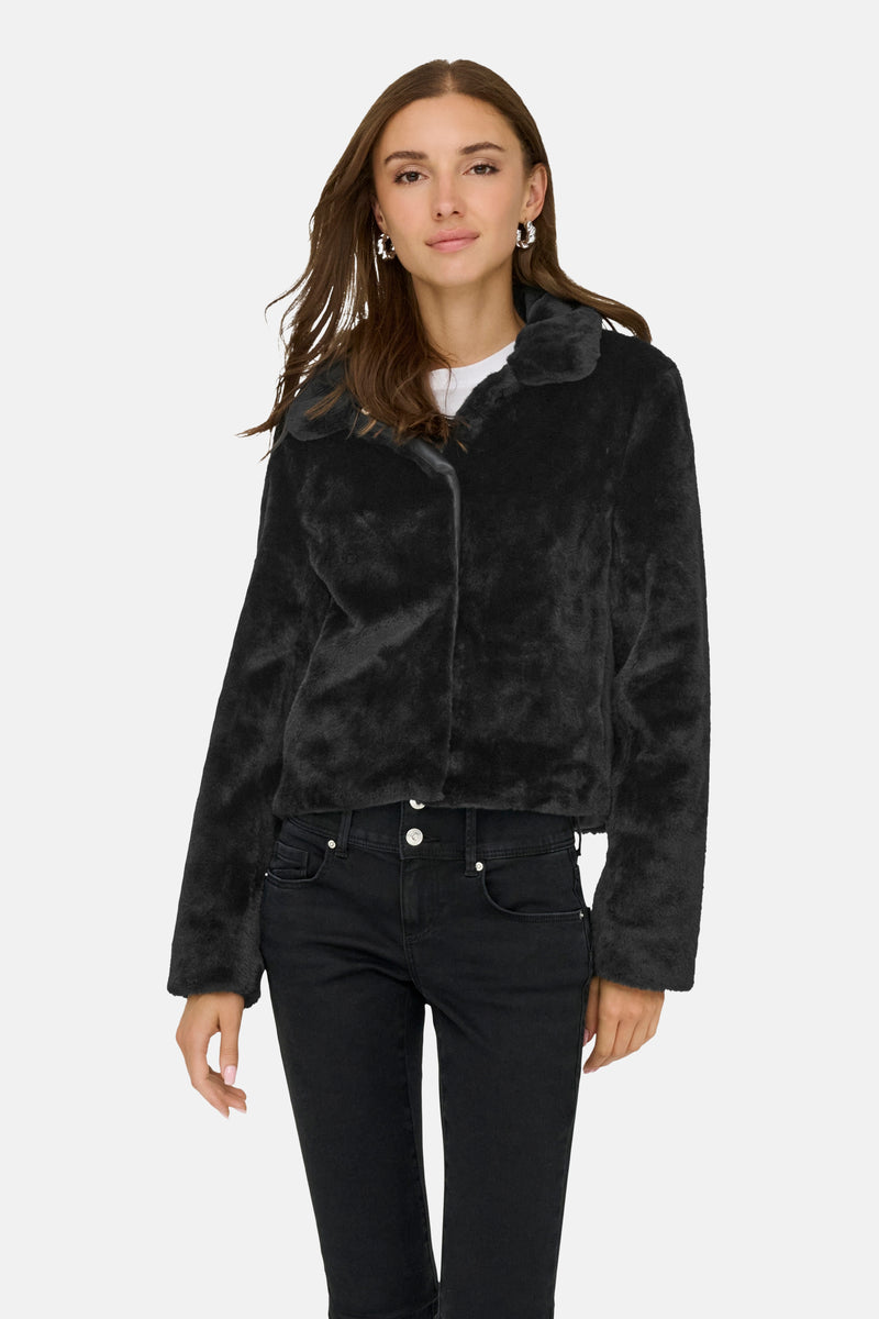 Veste courte noire en fausse fourrure de JDY, portée avec un t-shirt blanc et un jean noir.