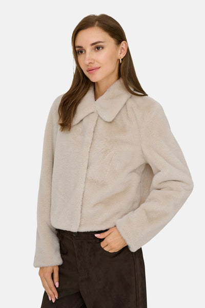 Veste courte beige de JDY, portée avec un pantalon marron en daim et des boucles d'oreilles dorées.
