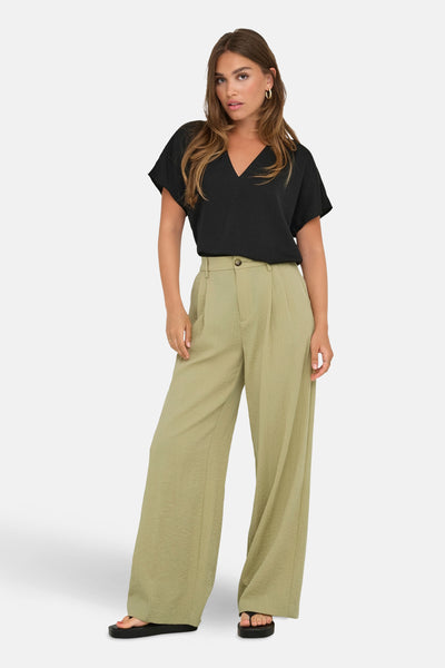 Pantalon de costume beige de JDY, coupe ample, texture froissée, porté avec un haut noir et des sandales.
