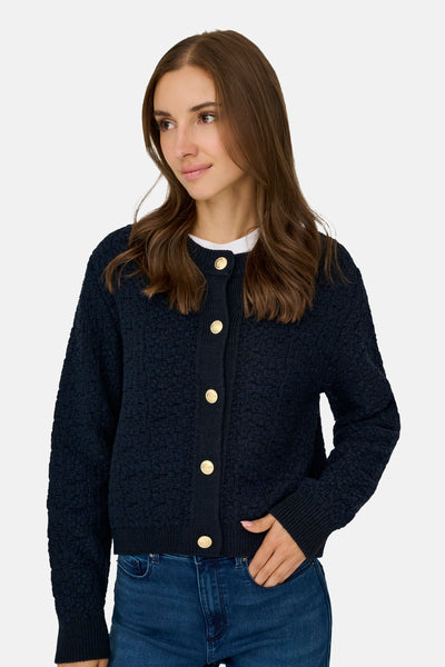 Cardigan bleu texturé by JDY, avec une fermeture boutonnée dorée, porté avec un t-shirt blanc et un jean.
