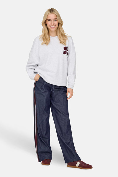 Donkerblauwe denim broek van ONLY, met een rood-witte zijstreep, gedragen met een grijze sweater.