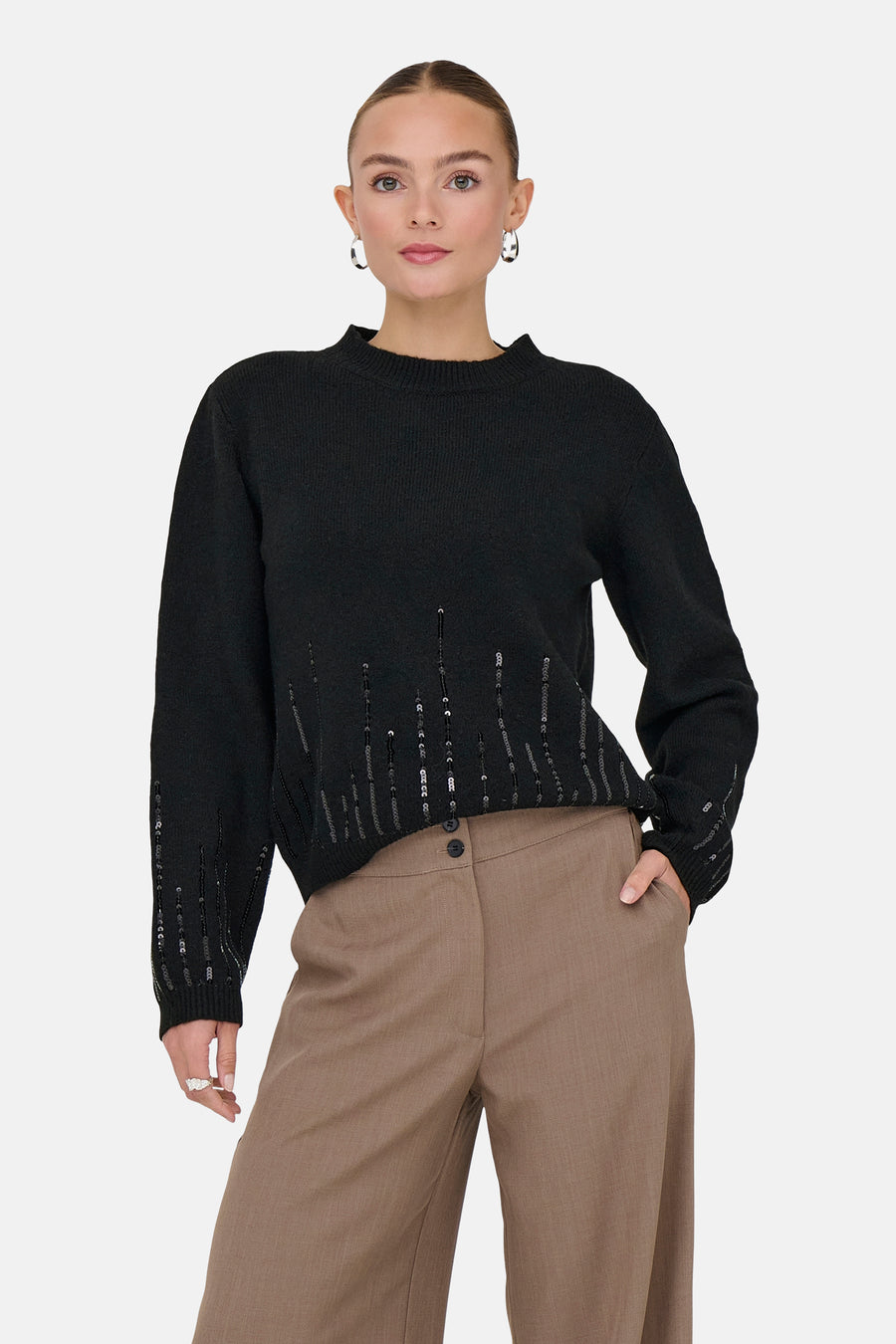 Pull à col rond noir par JDY avec des motifs de sequins et porté avec un pantalon marron.
