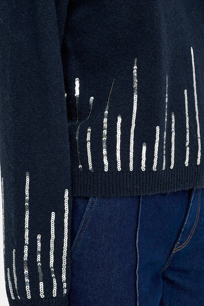 Pull à col rond bleu de JDY avec des rangées verticales de sequins argentés, porté avec un jean bleu foncé.