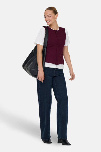 Bordeaux geribd mouwloos top met rits van JDY, gedragen over een wit T-shirt met een wijde jeans en een zwarte tas.