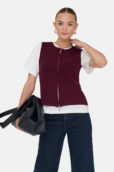 Bordeaux hemd zonder mouwen met ritssluiting van JDY, gedragen over een wit T-shirt, met een spijkerbroek en een zwarte tas.