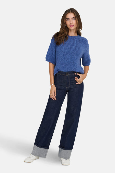 Wijde donkerblauwe jeans van JDY, met wijde zomen en witte sneakers.