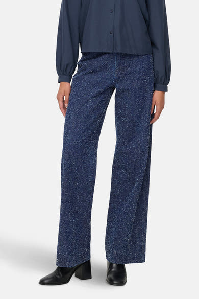 Gekleurde blauwe jeans van JDY, met wijde pijpen en gespikkeld patroon, gedragen met een blauw overhemd en zwarte enkellaarsjes.