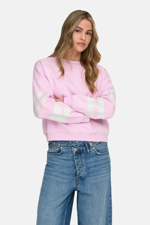 Sweat rose de ONLY, avec des manches longues décorées de rayures blanches, porté avec un jean bleu.
