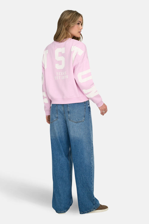 Sweat rose de ONLY®, avec un imprimé université au dos, porté avec un jean ample et des chaussures marron.
