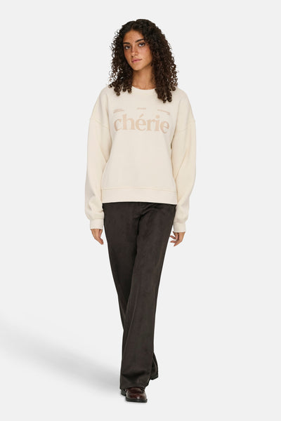 Sweat beige col O de ONLY®, porté avec un pantalon foncé et des chaussures marron.
