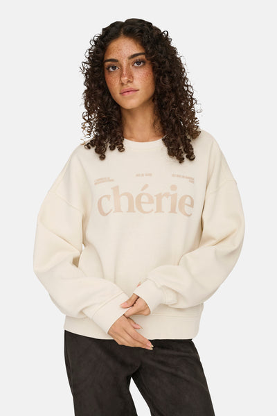 Sweat-shirt beige de ONLY, avec inscription décorative sur le devant, porté avec un pantalon foncé.
