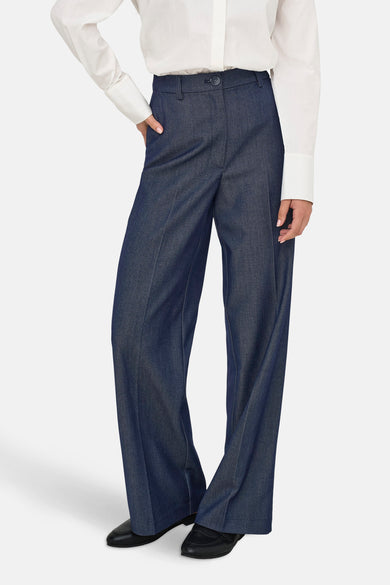 Donkerblauwe pantalon van pakstof van JDY, gedragen met een wit overhemd met lange mouwen.