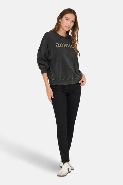 Zwarte rondehals sweatshirt van ONLY, met luipaardprint 'liefde' op de voorkant, gedragen met een zwarte jeans en witte sneakers