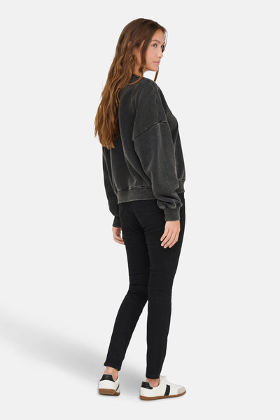 Zwarte rondehals sweatshirt van ONLY, gedragen met een strakke zwarte jeans en witte sneakers.
