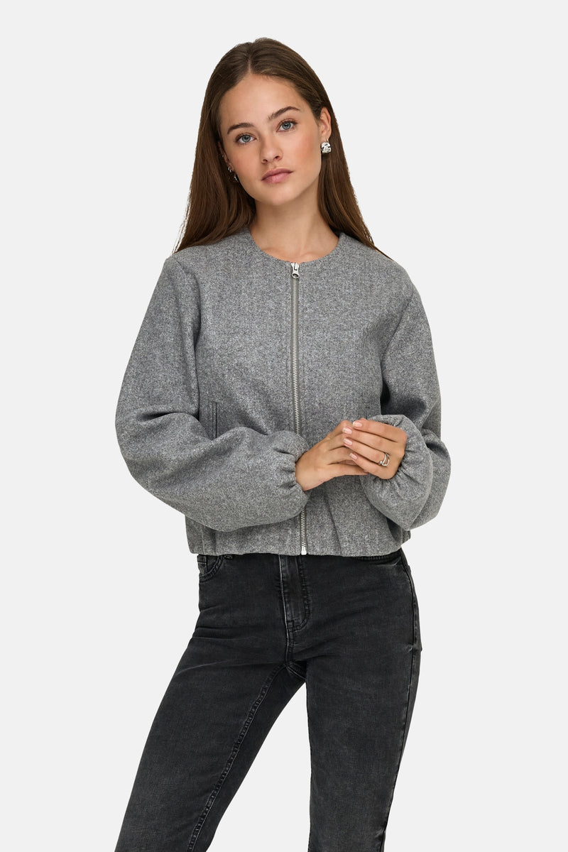 Korte grijze jas van JDY, met zilveren ritssluiting en gedragen met een zwarte jeans.