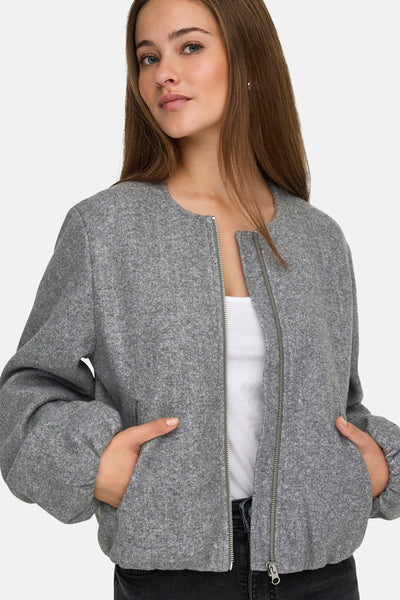 Veste courte grise de JDY, avec fermeture éclair et poches, portée sur un t-shirt blanc uni et un jean noir.
