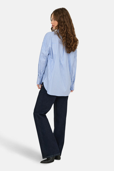 Blauwe blouse met lange mouwen van JDY, met verticale strepen, gedragen met een donkerblauwe bootcut jeans en zwarte enkellaarsjes.