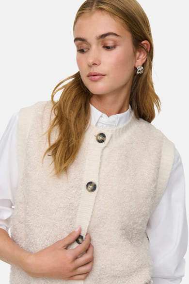 Débardeur écru by JDY, avec texture bouclée et boutons foncés, porté sur une chemise blanche à col boutonné.