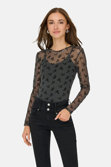 Grijze T-shirt met lange mouwen van JDY, zwart bloemenpatroon op doorschijnende stof, gedragen met een zwarte high-waist jeans.