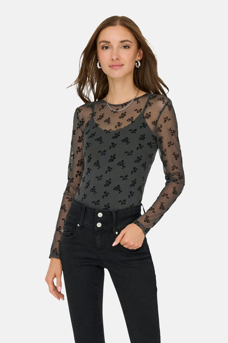 Grijze T-shirt met lange mouwen van JDY, zwart bloemenpatroon op doorschijnende stof, gedragen met een zwarte high-waist jeans.