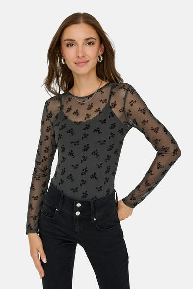 Grijze T-shirt met lange mouwen van JDY, met een zwart bloemenpatroon, gedragen met een zwarte high-waist jeans en zilveren oorbellen.