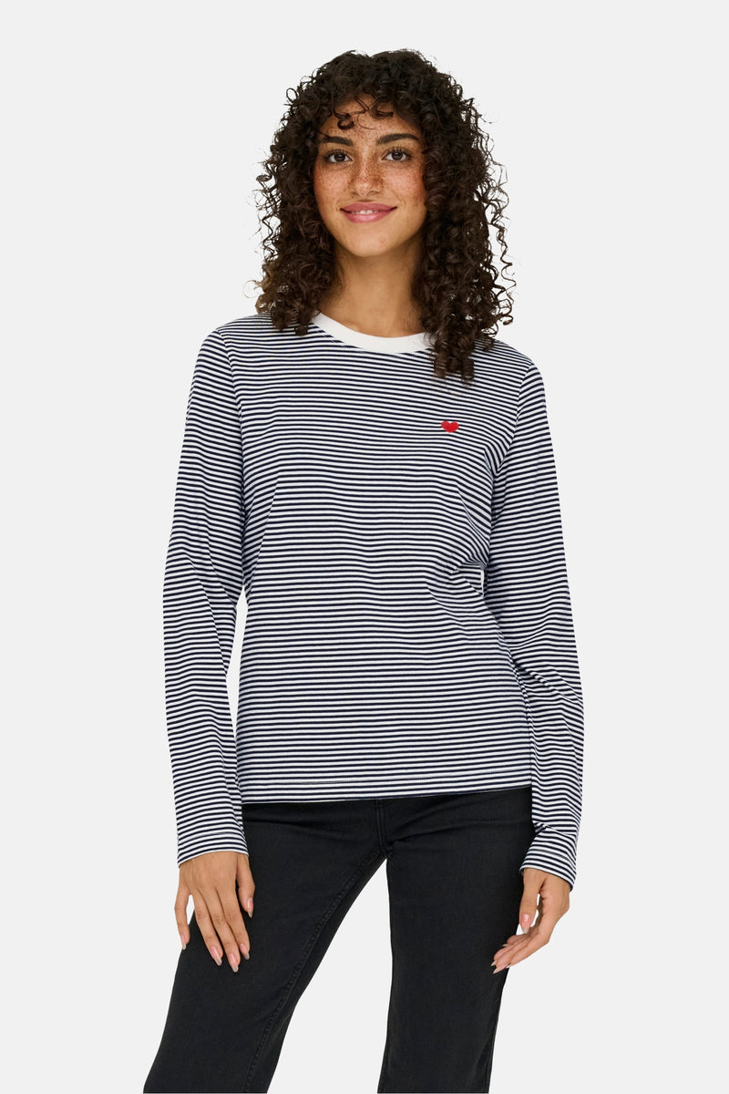 T-shirt à manches longues bleu rayé de JDY avec un petit cœur rouge brodé sur le devant, porté avec un jean noir.
