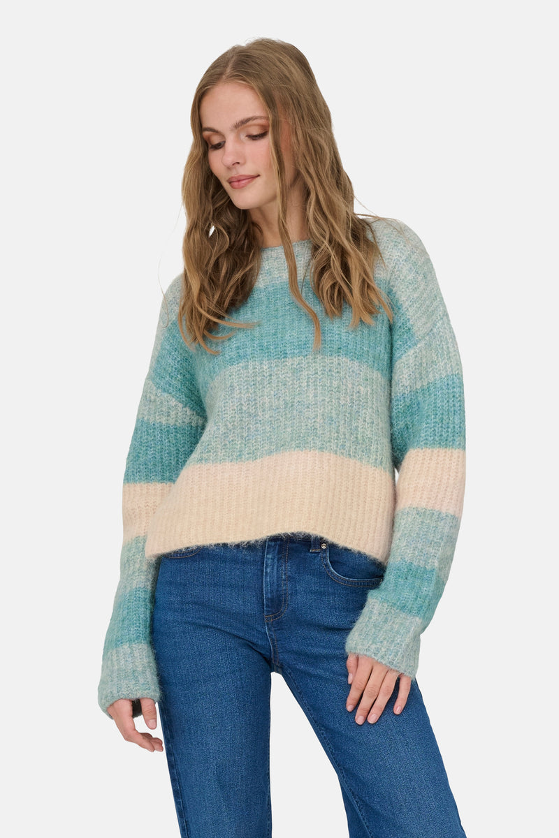Pull col rond bleu de JDY, à rayures turquoise et crème, porté avec un jean en denim.
