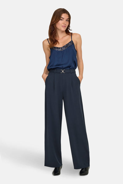 Pantalon bleu de JDY, coupe ample avec une ceinture décorative et porté avec un caraco bleu marine.
