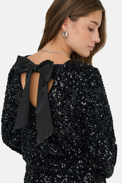 Zwarte blouse met lange mouwen van ONLY, met blote rug en grote decoratieve strik, gedragen met een zilveren ketting.