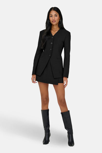 Blazer noir de ONLY, porté avec une jupe courte et des bottes hautes en cuir.
