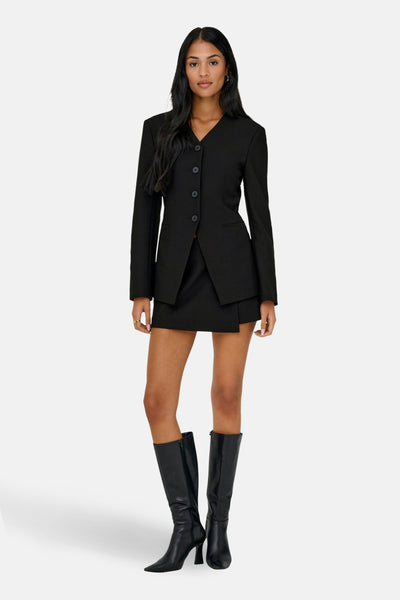 Short-jupe noir de ONLY®, porté avec un blazer noir et des bottes hautes en cuir noir.