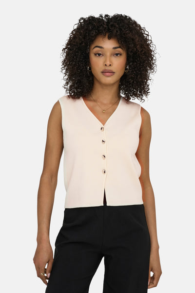 Gilet écru de JDY, avec des boutons et porté avec un pantalon noir taille haute.
