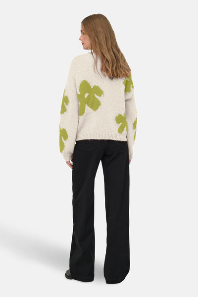 Pull col rond en tricot beige à motif fleuri vert de ONLY, porté avec un pantalon noir ample.
