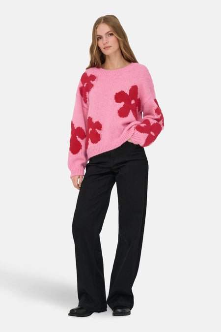 Pull rose à fleurs rouges de ONLY, porté avec un pantalon noir.
