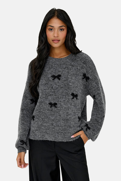Grijze trui met ronde hals van ONLY, versierd met zwarte knoopmotieven, gedragen met een zwarte broek.