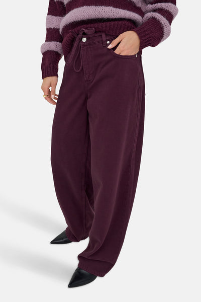 Jeans coloré bordeaux de ONLY, avec cordon de serrage et porté avec un pull rayé.
