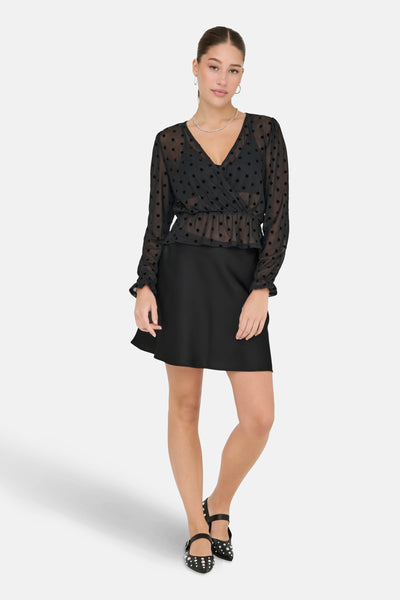 Zwarte korte rok van ONLY, effen, gedragen met een zwarte polkadot blouse en platte schoenen.