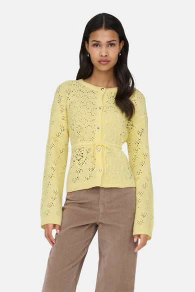 Geel vest van ONLY met ajourpatroon, strikceintuur en lange mouwen, gedragen met een bruine corduroy broek.