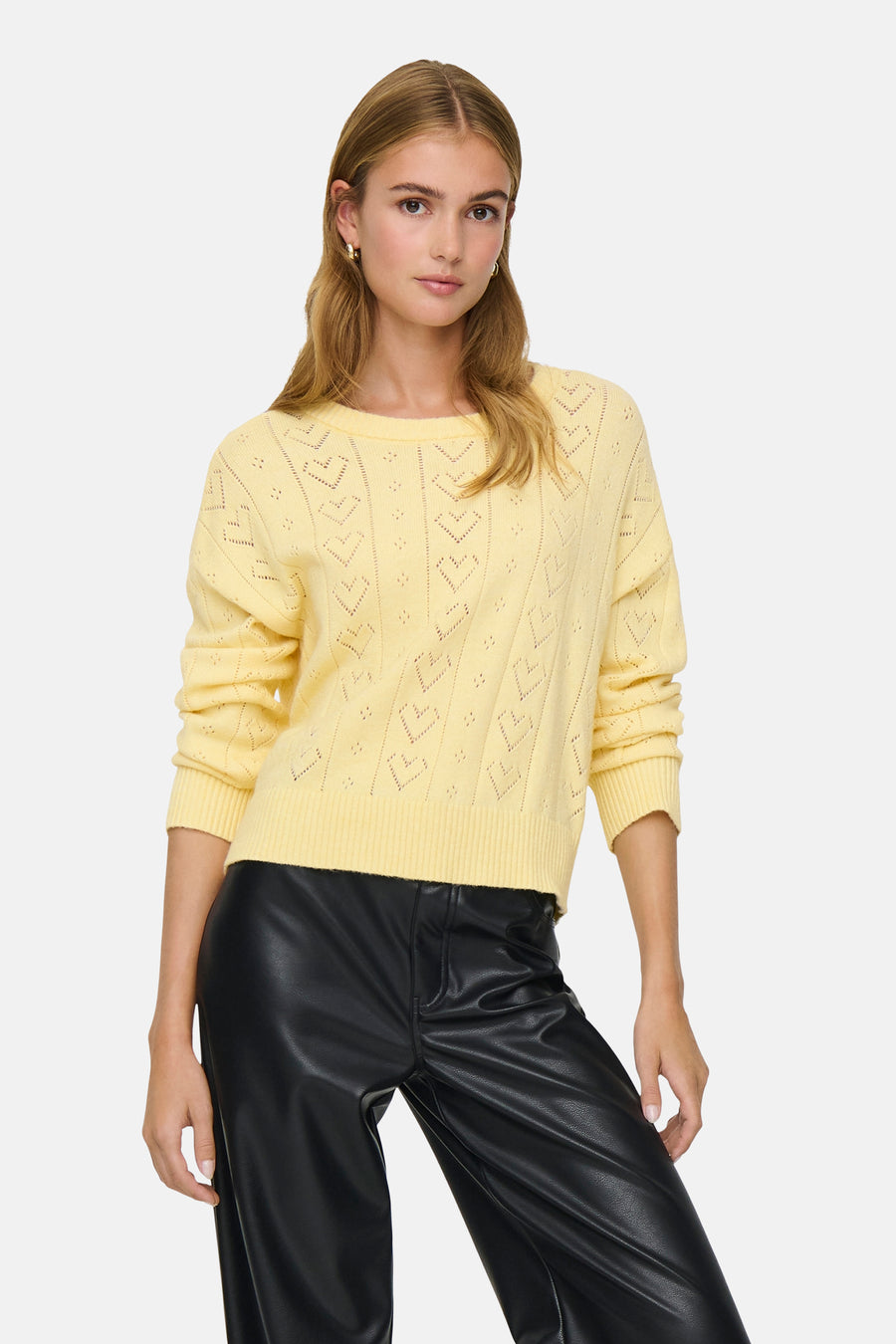 Ronde hals trui geel van ONLY® met ajourpatroon, gedragen met een zwarte imitatielederen broek.