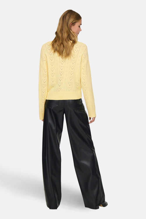 Pull à col rond jaune de ONLY, avec motif ajouré en forme de cœur, porté avec un pantalon noir large.
